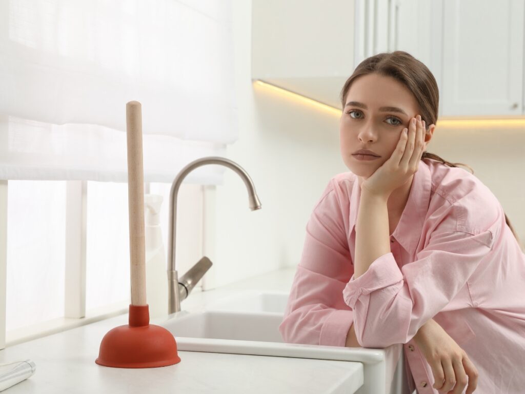 A woman laments over the kitchen sink plunger. Backflow testing in Long Island can prevent many headaches.