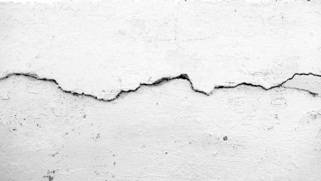 A deteriorating peeling white painted concrete wall showcases the effects of a slab leak. The cracked wall and water damage are evident, caused by leaking rainwater. The texture of the wall, with its peeling paint and rough surface, adds to the abandoned and vintage backdrop. This architectural detail highlights the importance of responsible construction, as well as the need for repair and fixing drainage issues. The moisture, dampness, and seepage have taken a toll on the integrity of the building's structure. This image serves as a reminder of the potential consequences of a slab leak, emphasizing the importance of prompt and reliable repair services to ensure a safe and healthy home or building environment.