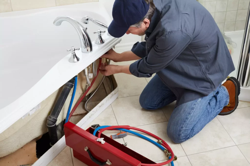 A plumber kneeling on a bathroom floor to fix bathtub faucet leaks.