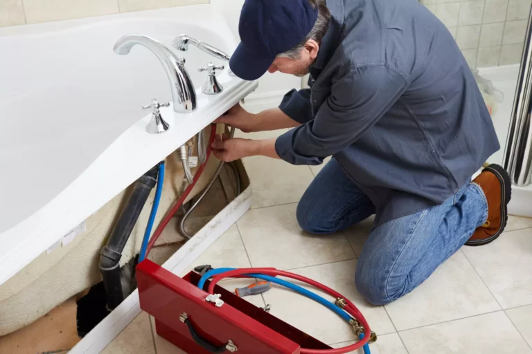 A plumber kneeling on a bathroom floor to fix bathtub faucet leaks.